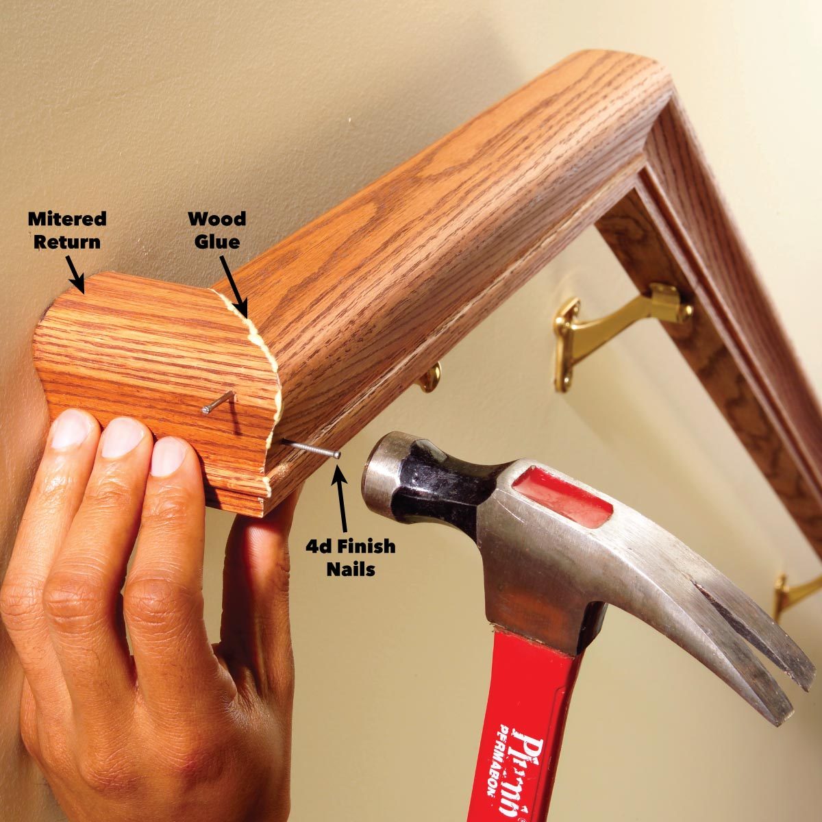 A hand holds a mitered return while hammering 4d finish nails into a wooden trim mounted on a wall in a home interior.