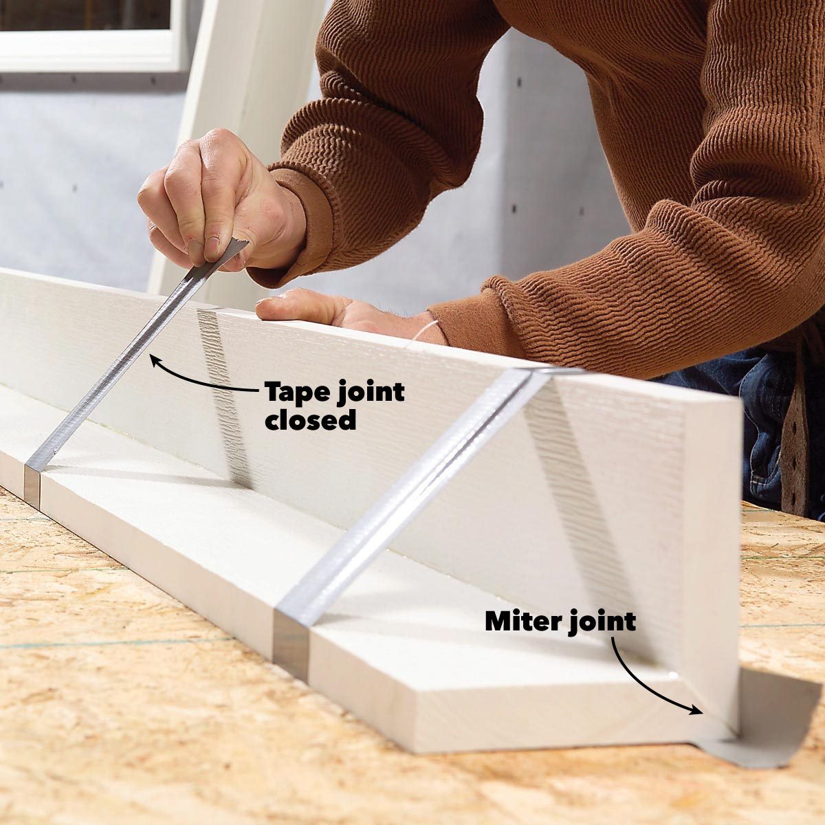 A person uses a tool to adjust joints on a wooden plank in a workshop, with labeled indications for "Tape joint closed" and "Miter joint."