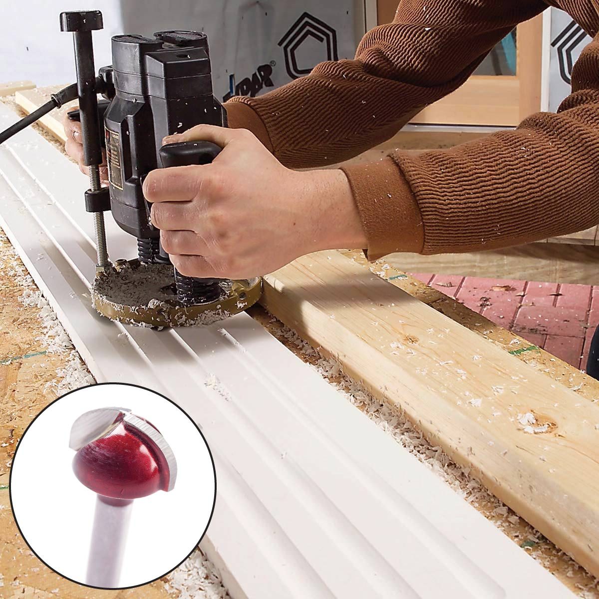 A person uses a router to shape a piece of wood, creating grooves, surrounded by wood shavings in a workshop setting.