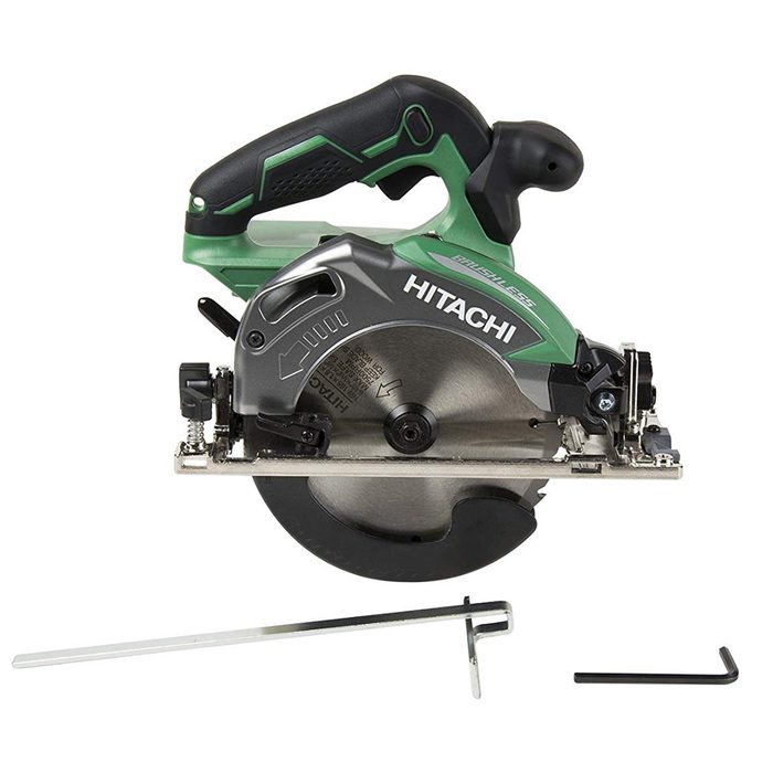 A circular saw with a green and gray handle is positioned on a flat surface, accompanied by two metallic tools for adjustments.