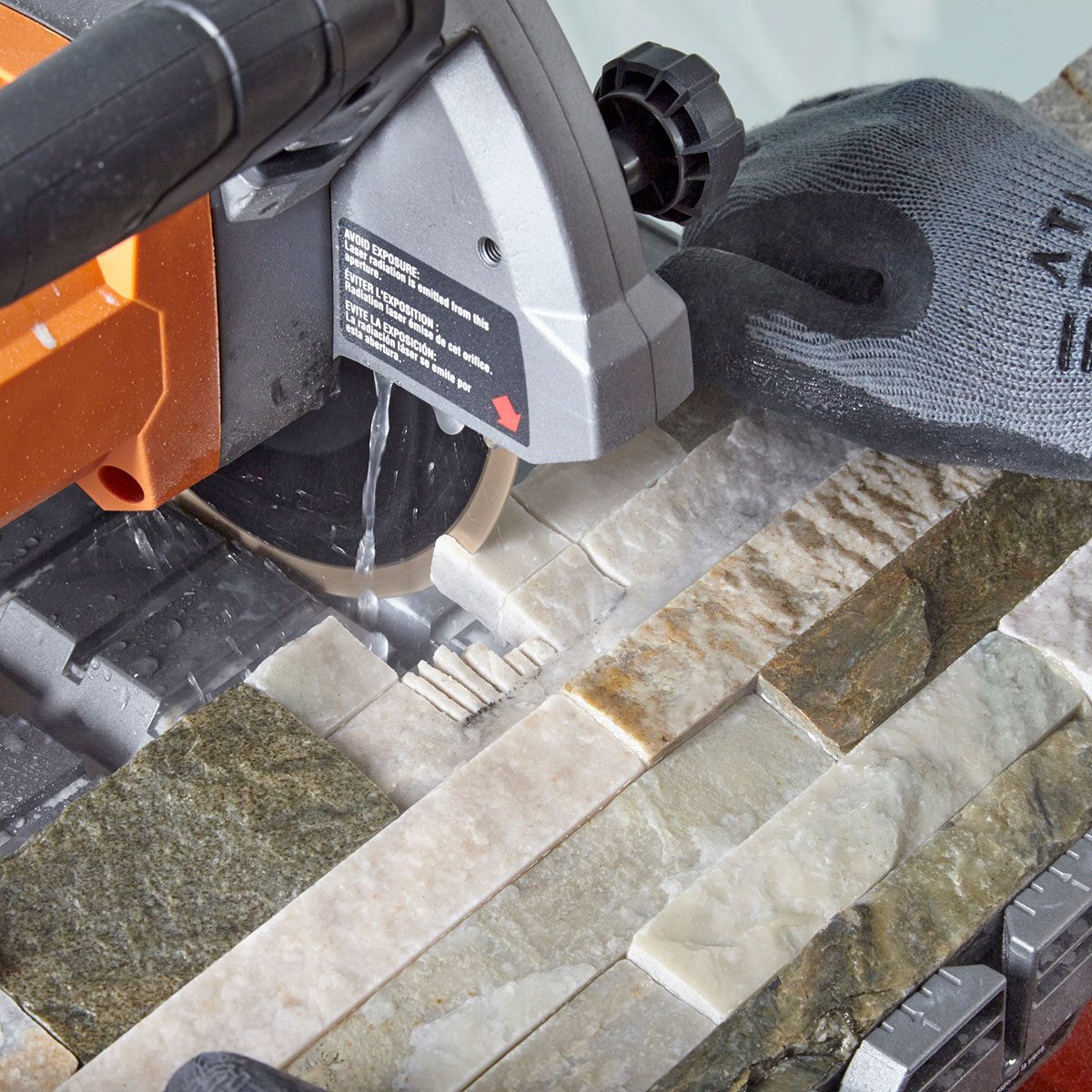 A wet saw cuts through stone tiles with a rotating blade, while a gloved hand carefully positions the material on a work surface.