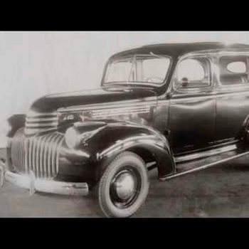 A vintage black car stands stationary, showcased against a light backdrop, highlighting its classic design and shiny chrome accents.