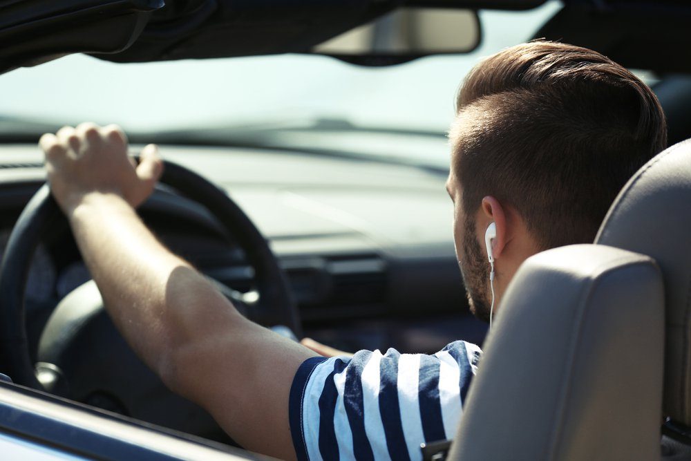 A person drives a car while listening to music, seated inside a vehicle with a soft-top roof, showing a clear view of the dashboard.