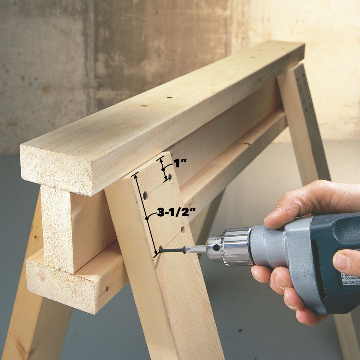 A hand holds a drill, fastening wood pieces on a sawhorse. Measurements marked on the wood guide the drilling process in a workshop setting.