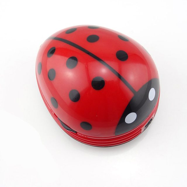 A red ladybug-shaped object rests on a white surface, featuring black spots and eyes, appearing playful and decorative in its presentation.