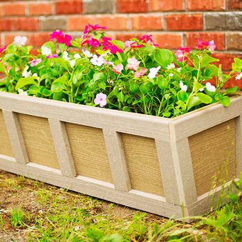 Colorful flowers bloom in a wooden planter, showcasing shades of pink and green, set against a textured red brick wall.