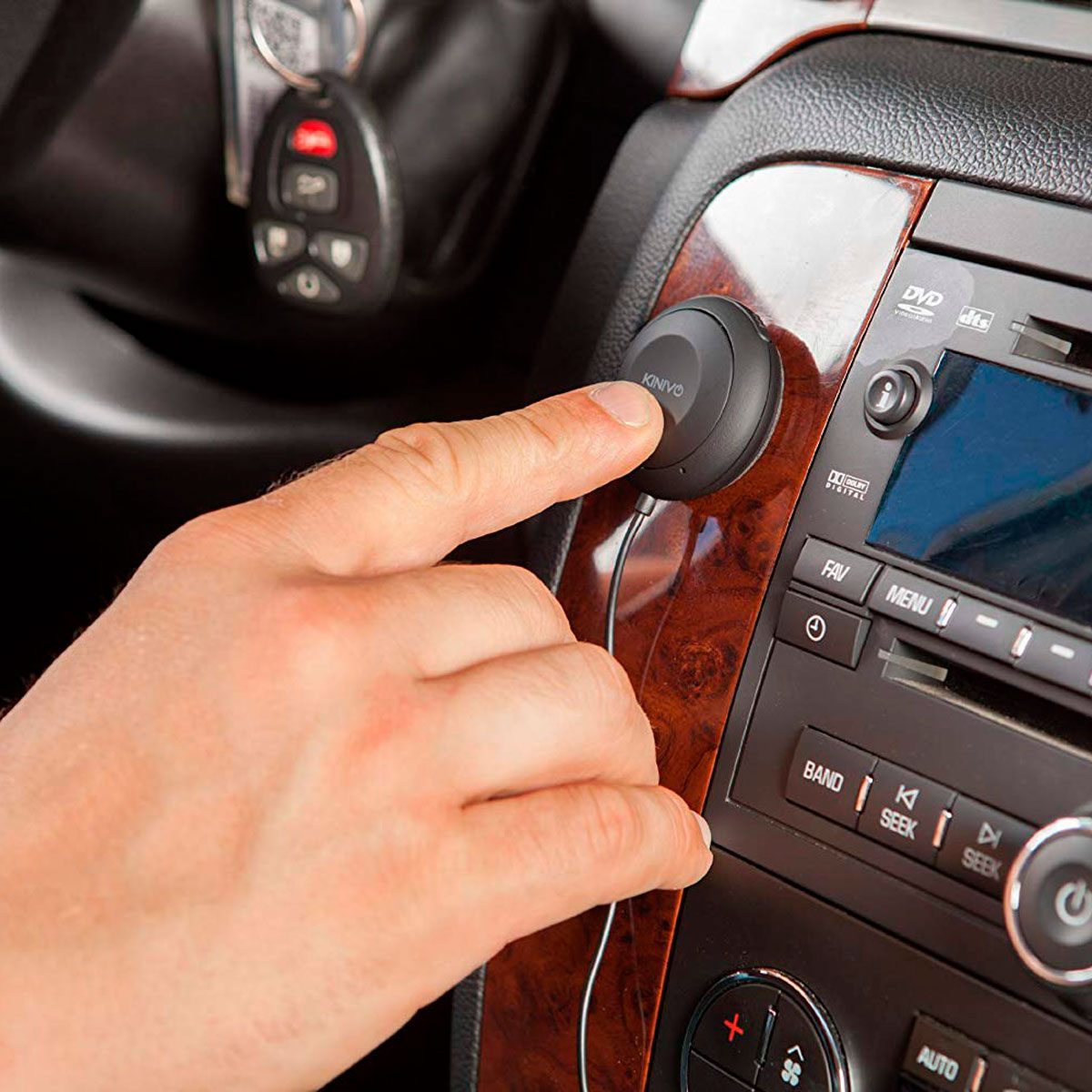 A hand presses a button on a car's dashboard, interacting with a device connected to the audio system in a vehicle's interior.