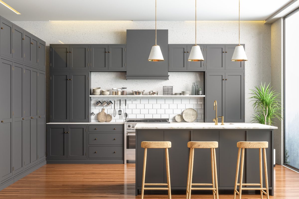A modern kitchen features dark cabinetry, a marble countertop island, and wooden stools, set against a bright window and sleek tile backsplash.