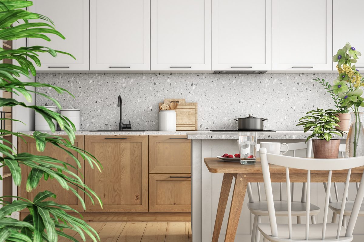 A wooden table with a glass of water and a plate of berries sits in a modern kitchen, featuring light cabinetry and a stone countertop.