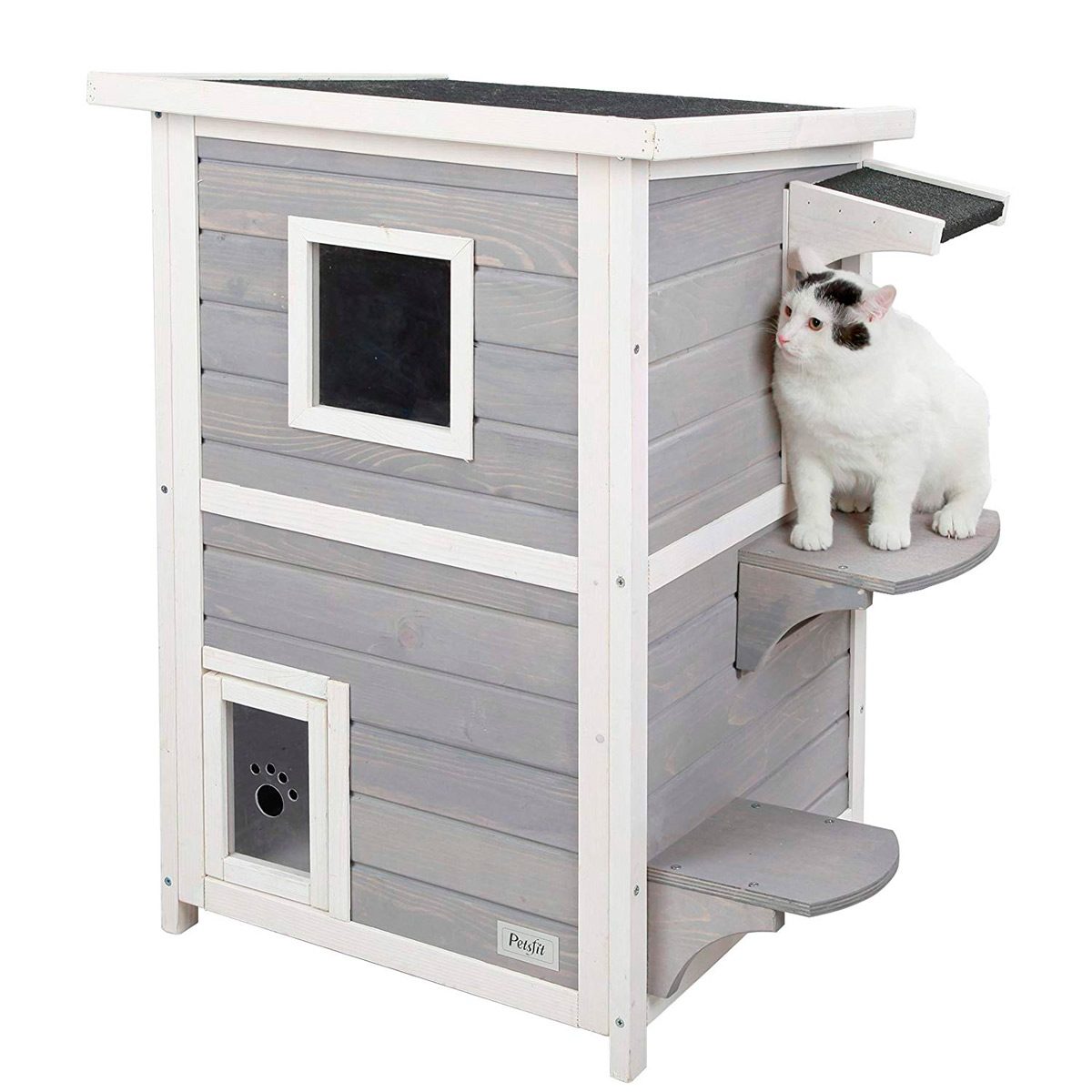A white cat sits on a shelf attached to a wooden cat house with gray and white panels, featuring a small entrance and a window.