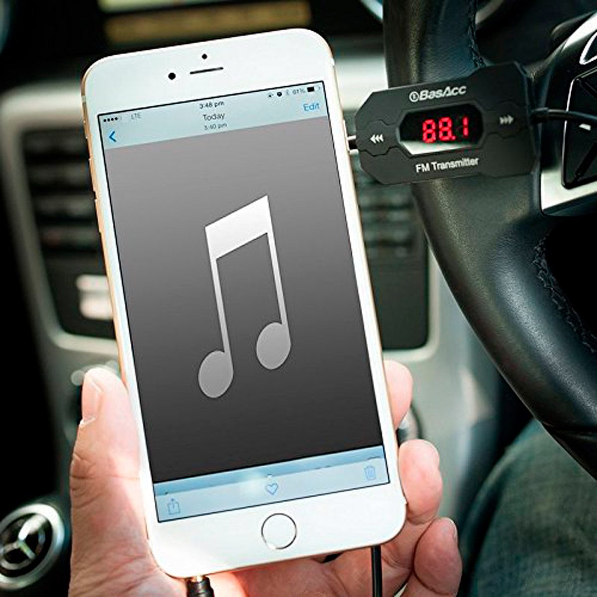 A hand holds a smartphone displaying a music note icon, connected to an FM transmitter in a car, suggesting music playback through the vehicle's audio system.