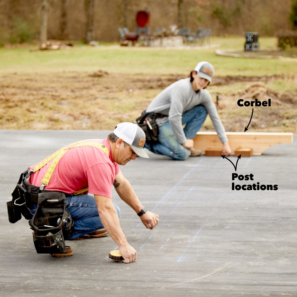 Two workers are measuring and marking post locations on a flat surface, surrounded by a grassy area with distant seated furniture.