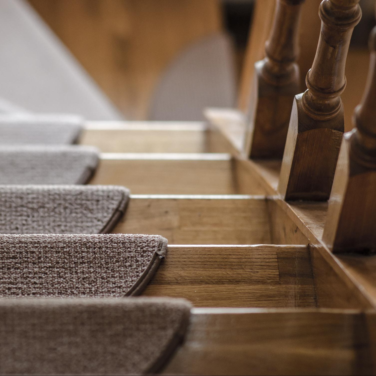 Carpeted stair treads are positioned on wooden steps, facilitating safe movement between levels in a well-lit indoor space. Banister posts are visible alongside.