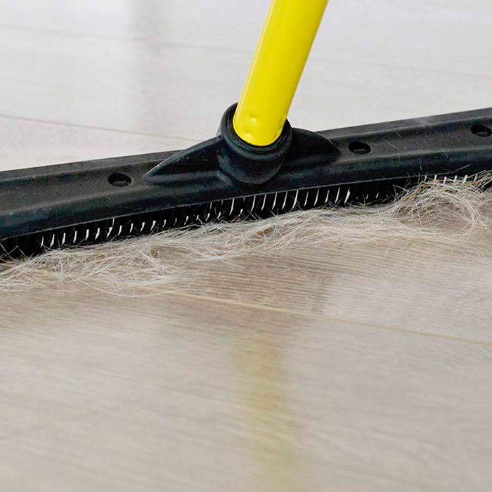A long-handled scrub brush with blue bristles is positioned upright, ready for cleaning a surface, typically found in a household or commercial setting.