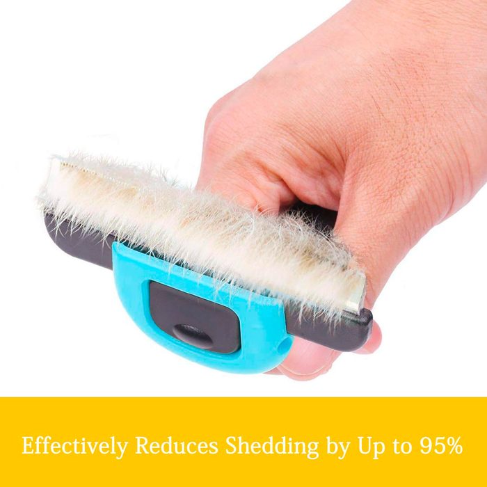 A hand grips a pet grooming brush, which has a soft bristle surface, positioned against a plain background.