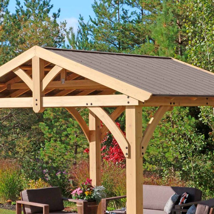 A wooden pergola stands upright, providing shelter. Colorful flowers and greenery surround it, creating a vibrant outdoor space for relaxation.