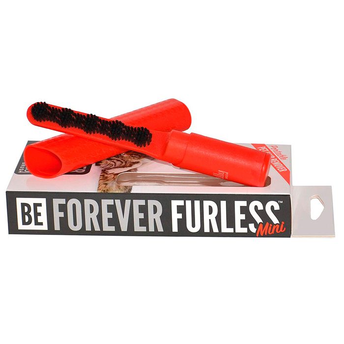 A red pet grooming tool rests on a black and white packaging, designed to remove fur from animals efficiently. Text on packaging reads: 