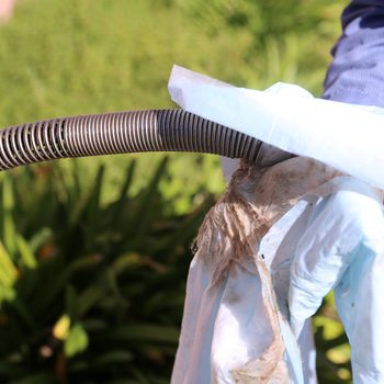 A hand wearing a blue glove holds a dirty, tangled hose, partially covered with a cloth, against a backdrop of green foliage.