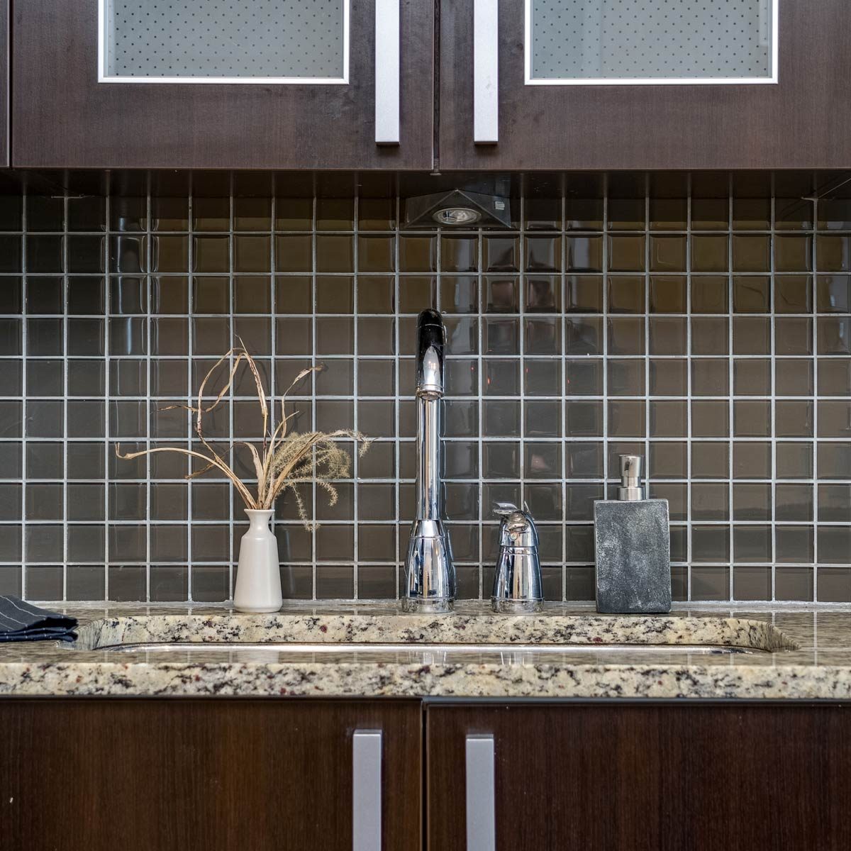 small square black tile backsplash above a kitchen counter with dark cabinets