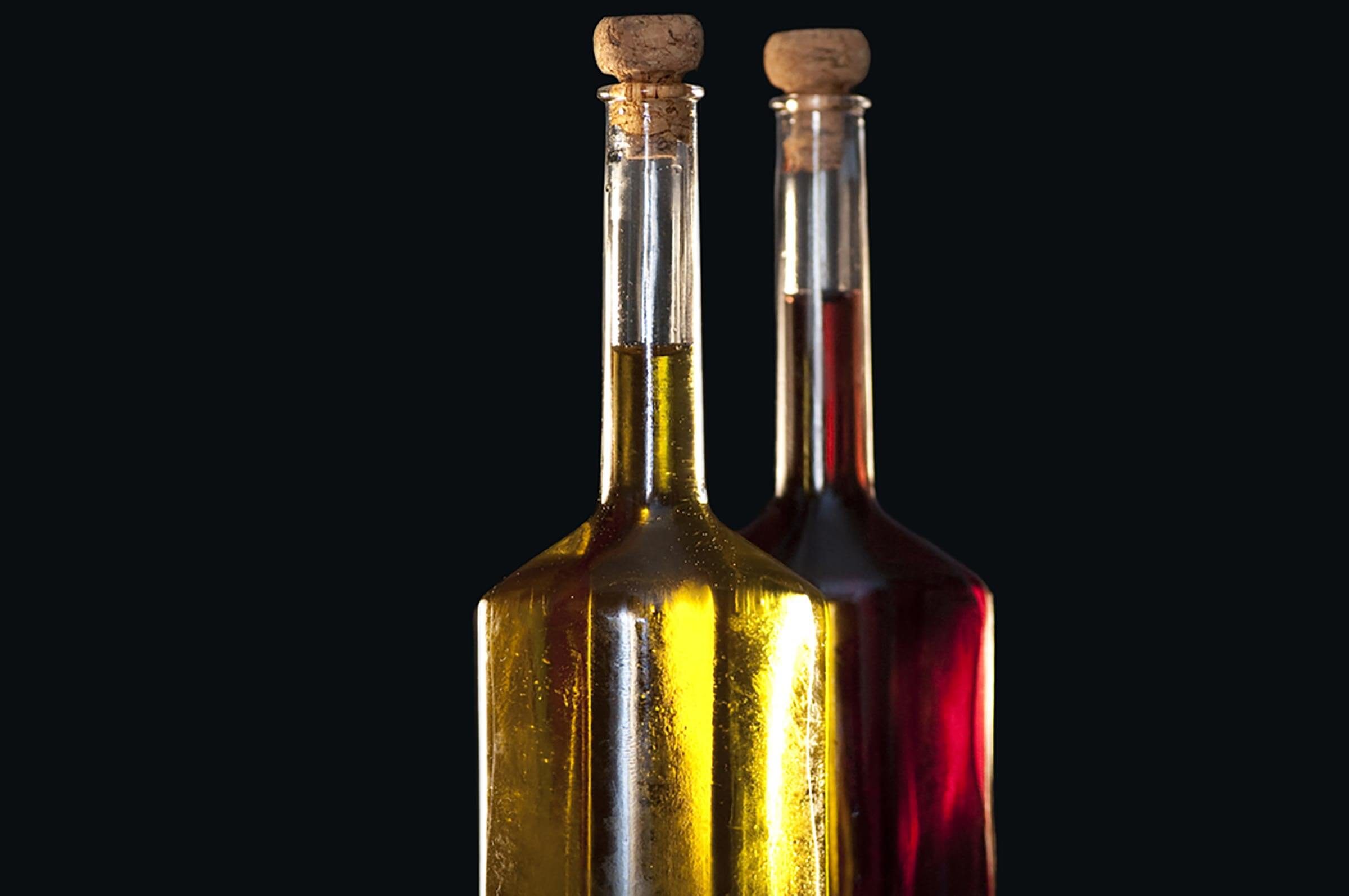 Two glass bottles filled with yellow and red liquids stand side by side, capped with corks, against a dark background.