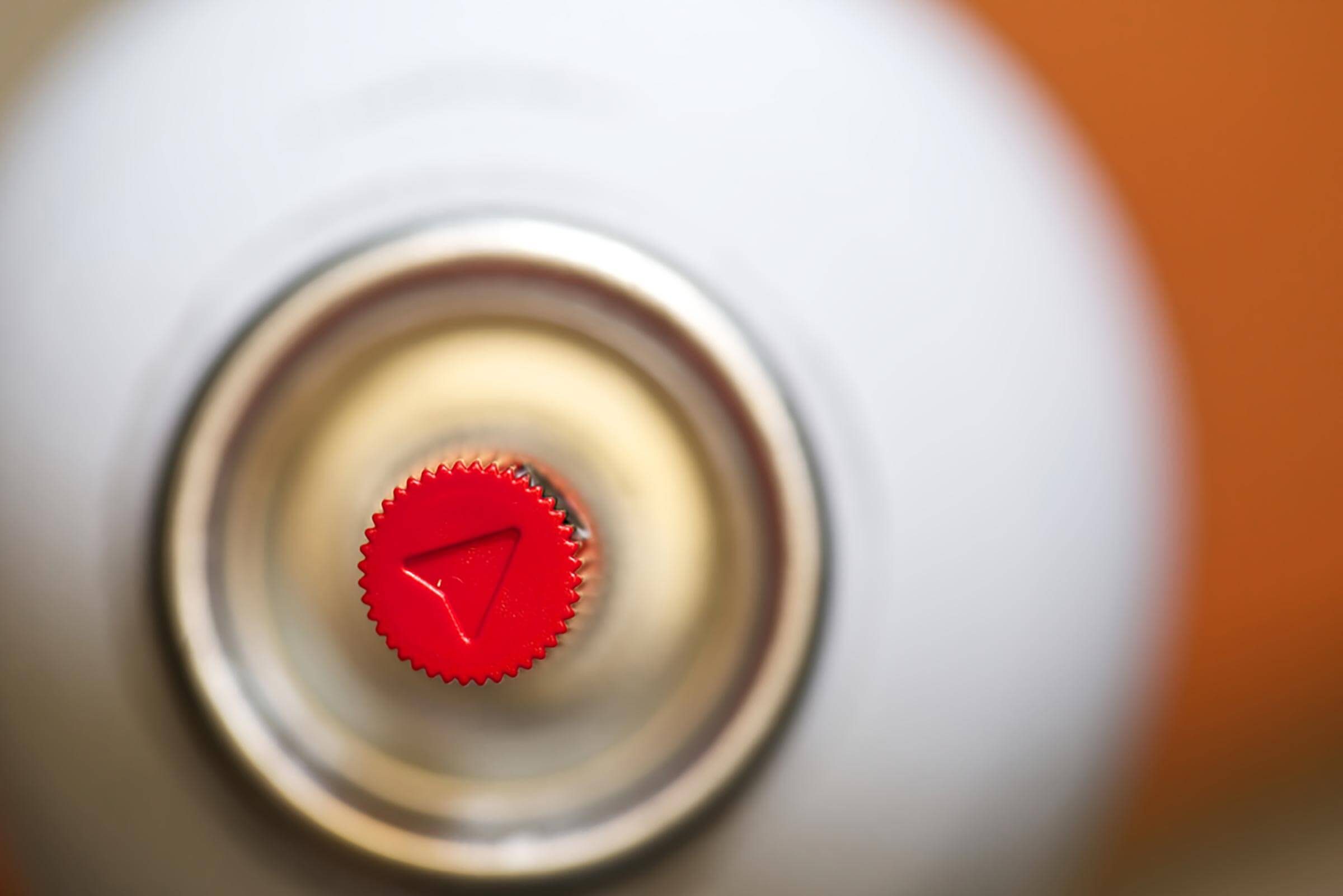 A red, triangular knob sits atop a metal canister, positioned centrally against a blurred background of neutral tones.