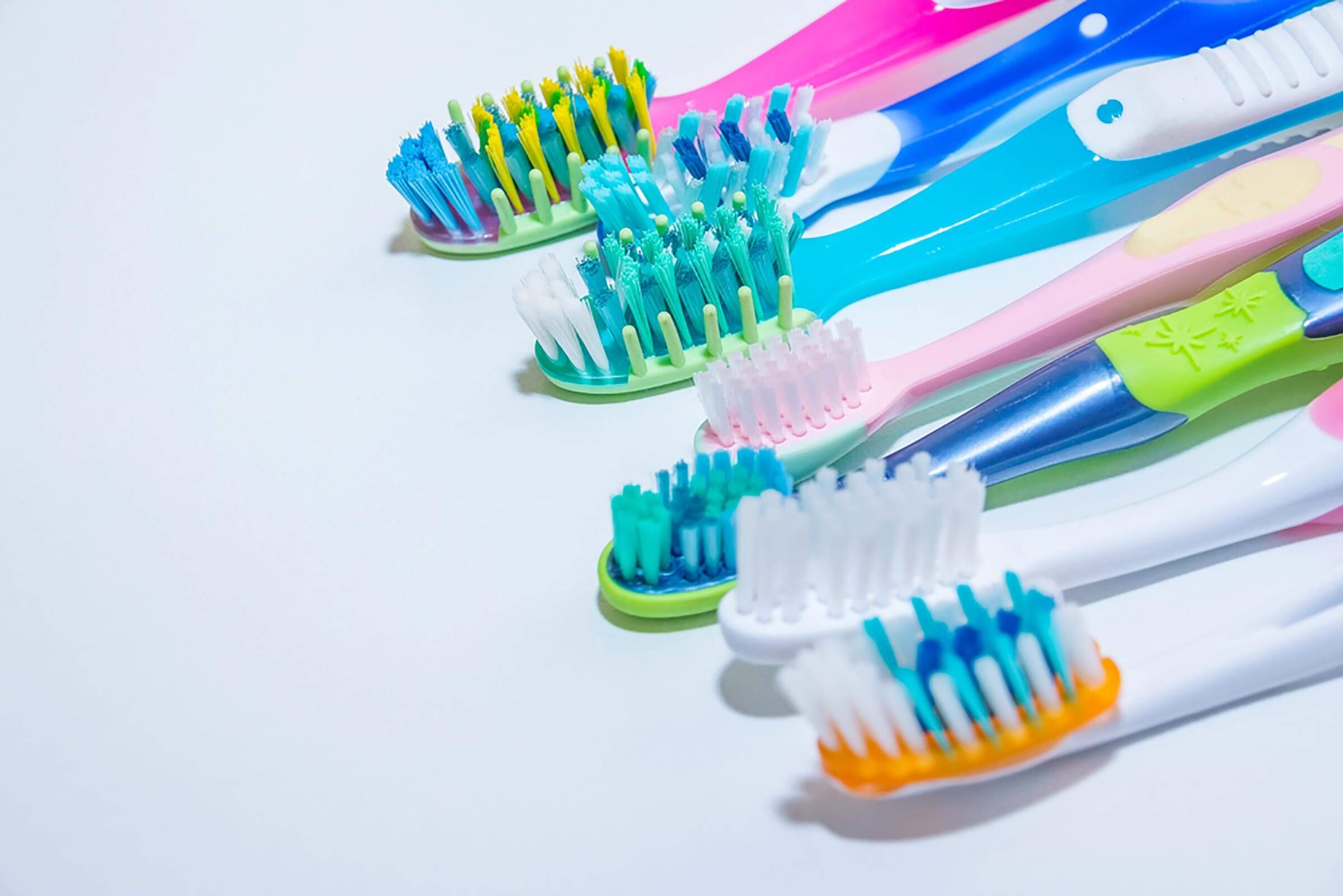 Colorful toothbrushes are arranged in a row, displaying various bristle styles and colors, set against a simple white background.