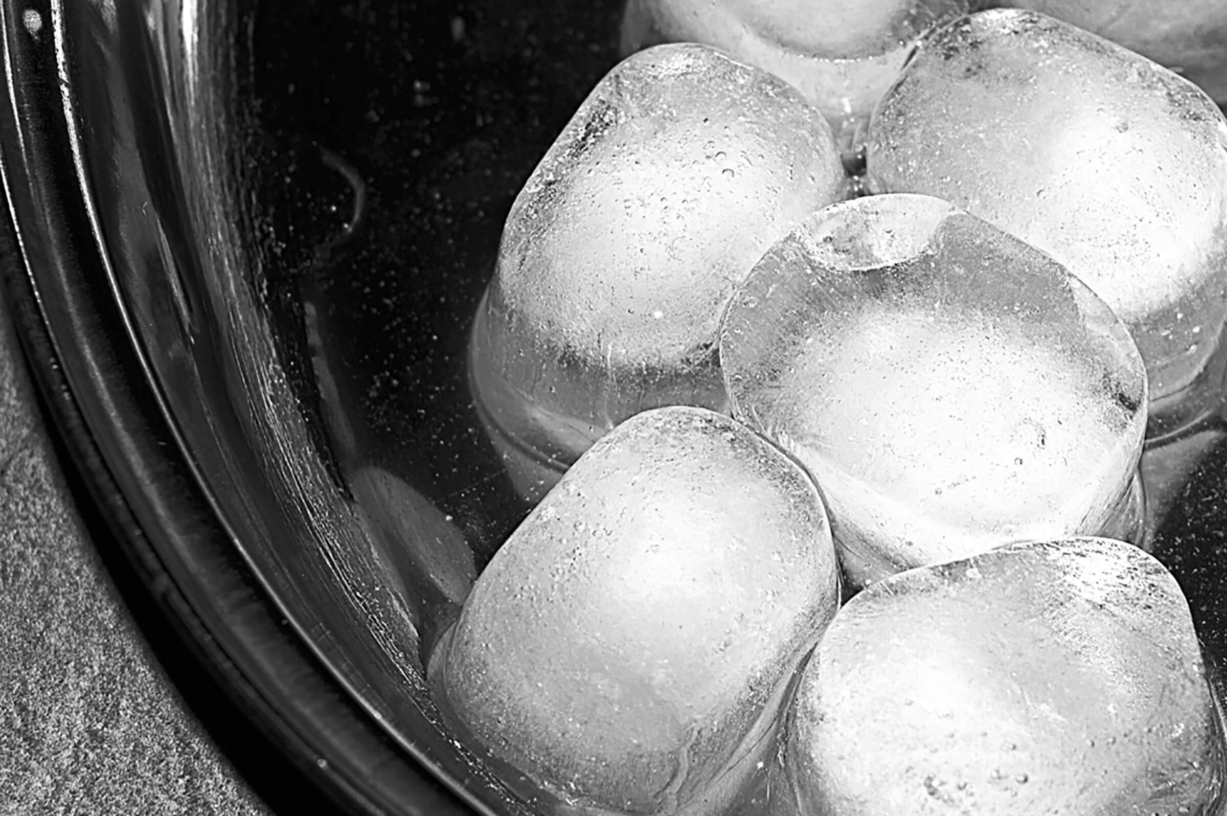 Ice cubes fill a round container, partially submerged in water, reflecting light. The surface shows condensation, indicating a cold temperature.