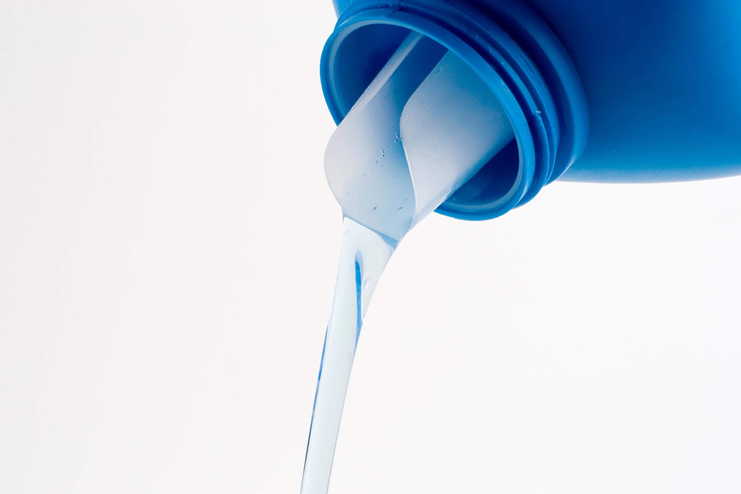 A blue bottle pours a clear liquid downward, surrounded by a plain white background, emphasizing the flowing movement of the liquid.