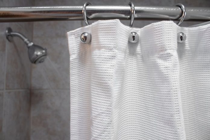 a white shower curtain in an empty shower with water OFF closeup shot