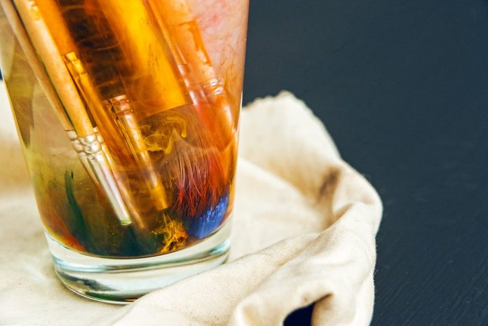 Artistic brushes soiled in paint soak in a glass with water