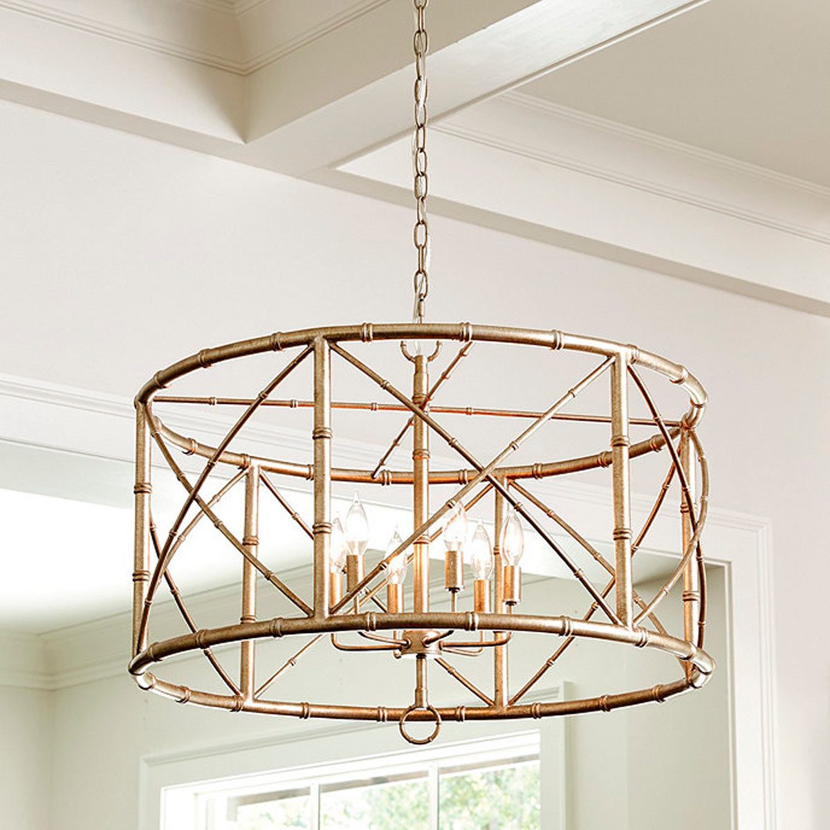 A cylindrical chandelier hangs from the ceiling, featuring a geometric metal frame with multiple light bulbs, illuminating a bright, open interior space.