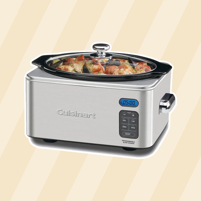 A stainless steel slow cooker is cooking a contents of meat and vegetables, displaying a timer set to five hours against a light striped background.