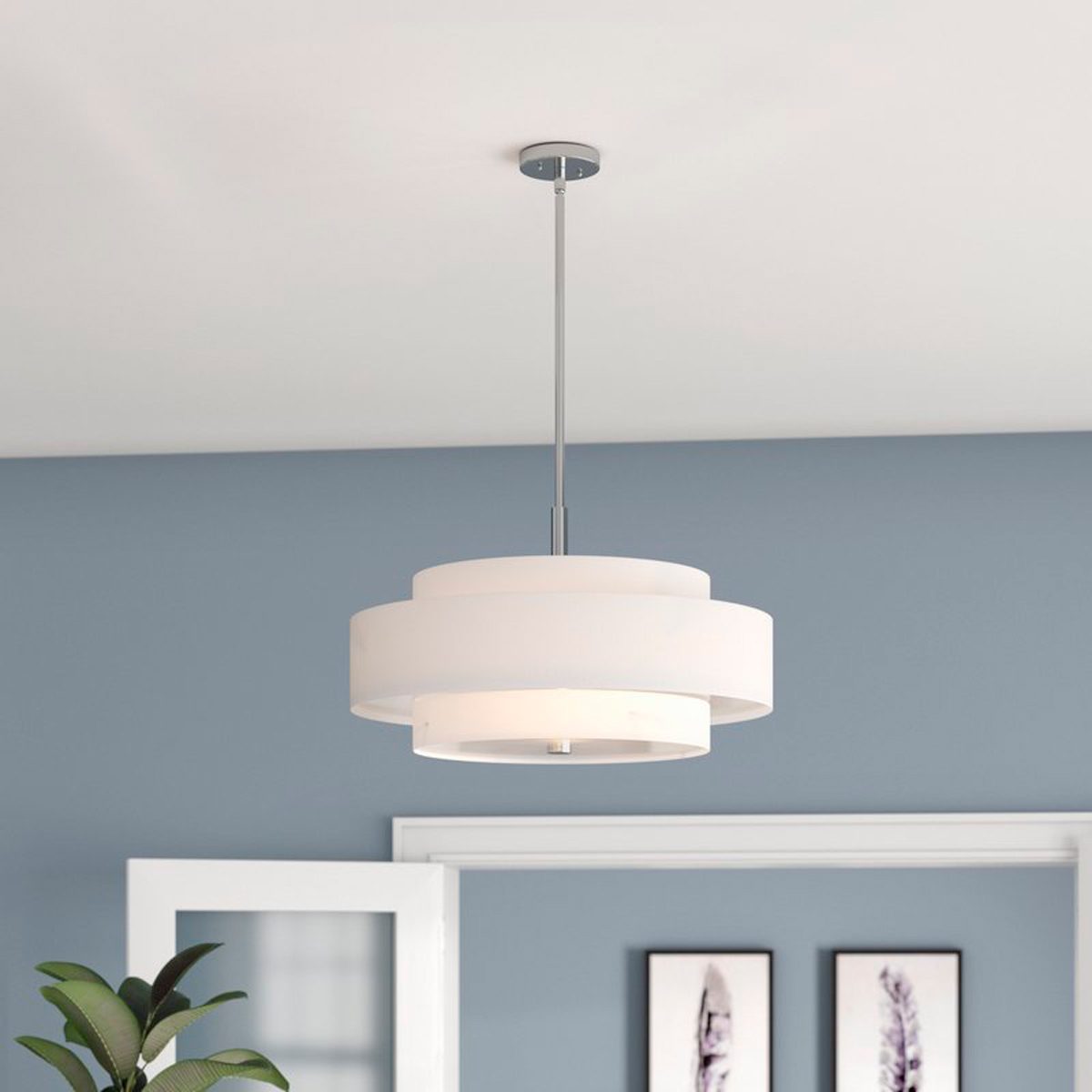 A circular pendant lamp hangs from the ceiling, illuminating a light blue room with framed feather prints and a green plant in a corner.