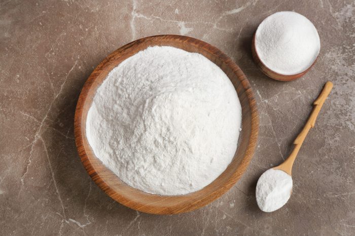 Bowls and spoon with baking soda on gray table, top view