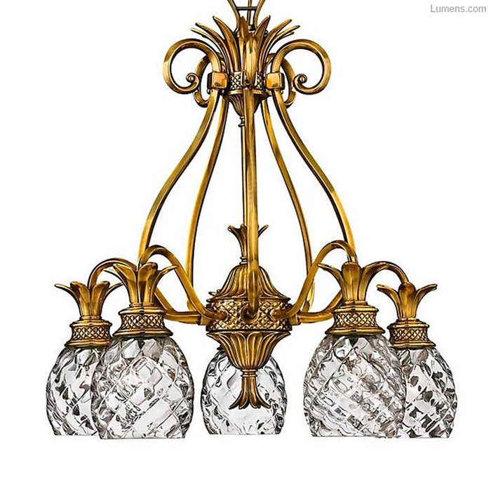 A decorative chandelier features five crystal glass shades shaped like pineapples, suspended from a gold-toned metal framework, adding elegance to a space.