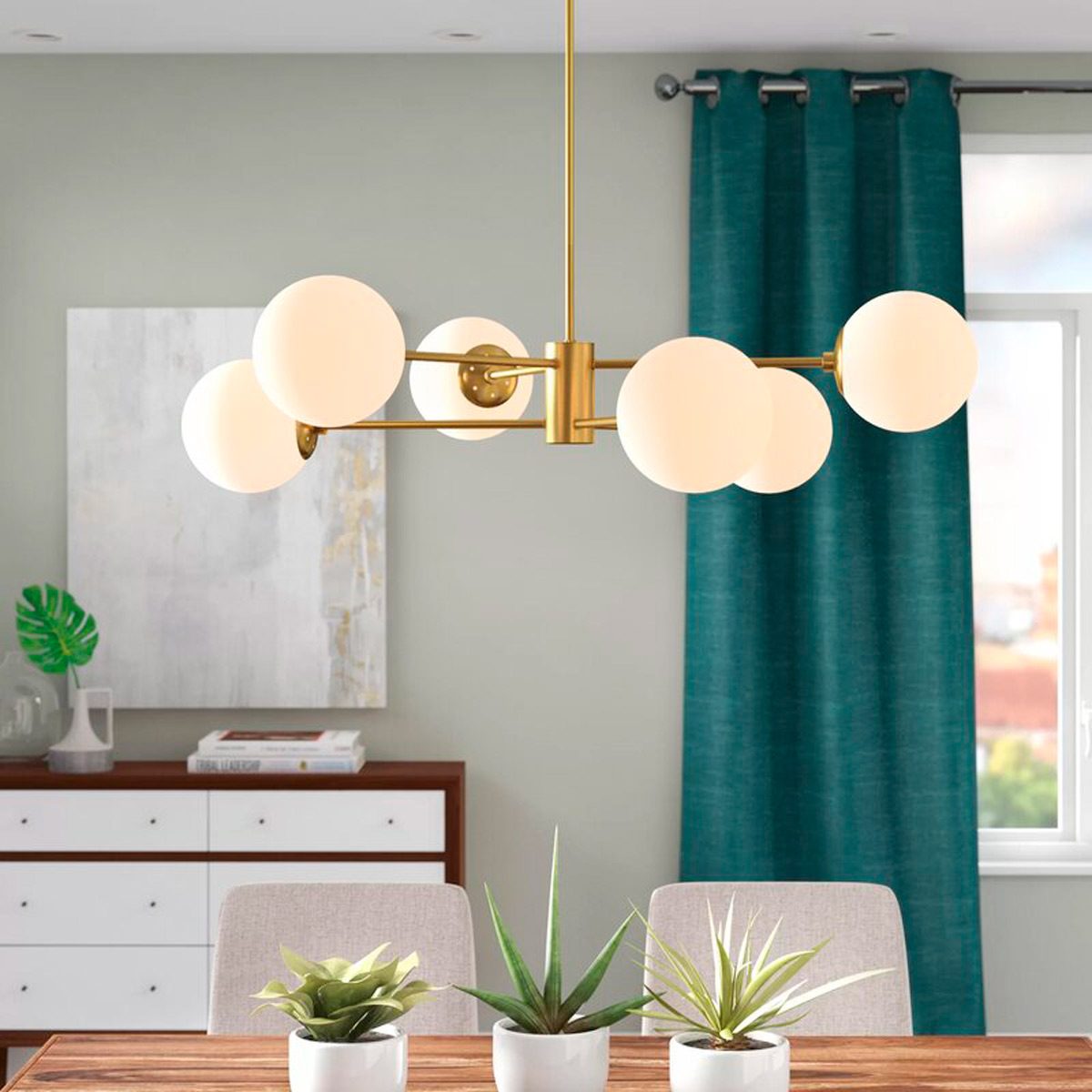 A modern chandelier with spherical white bulbs hangs over a dining table surrounded by potted plants, set against a soft green wall and teal curtains.