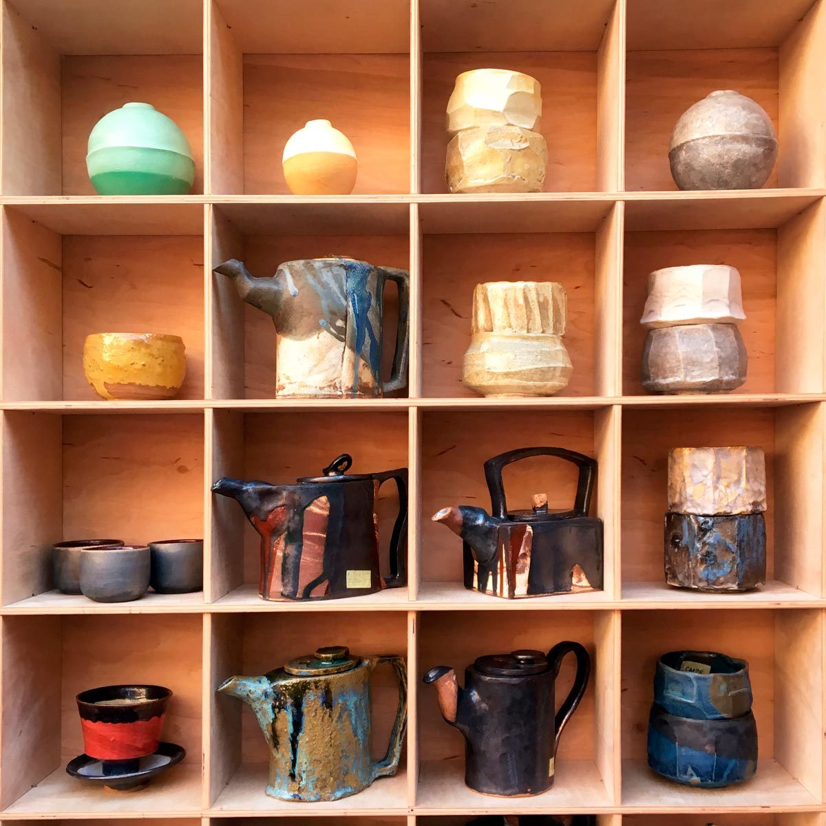 A collection of pottery pieces, including teapots and bowls, neatly arranged in a wooden display case, showcasing various colors and textures.