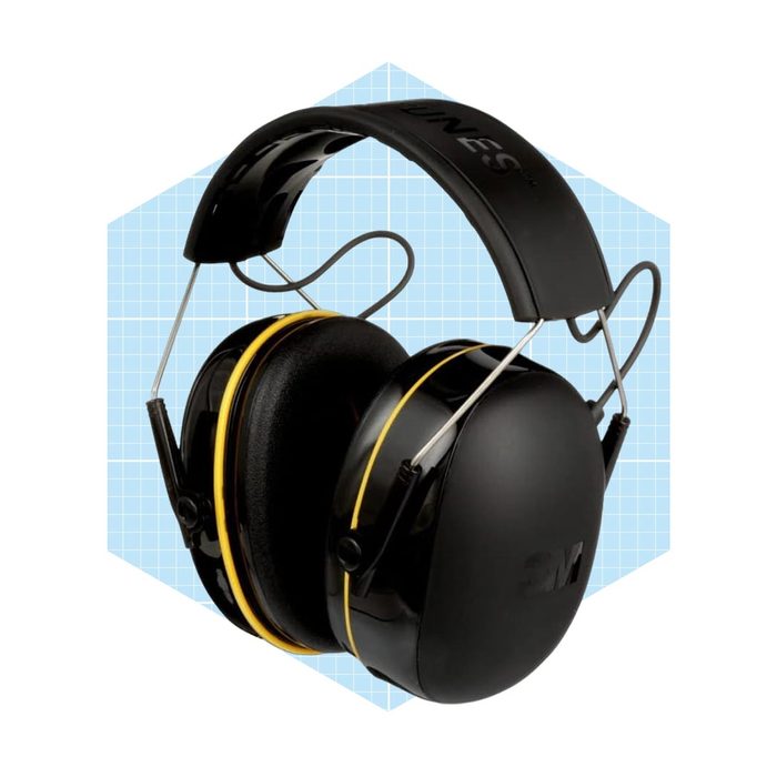 Black protective headphones with yellow accents rest upright against a light blue patterned background, designed to muffle sound in noisy environments.