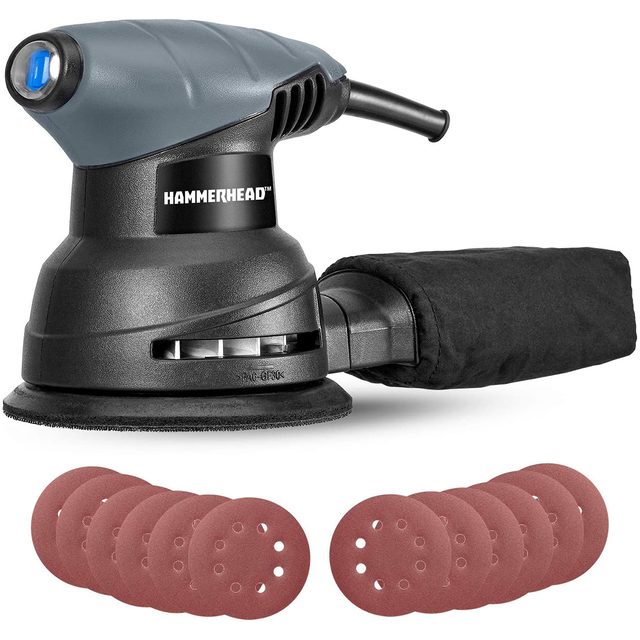 A handheld sander is resting on a surface, accompanied by multiple sanding discs, ready for use in woodworking or finishing tasks.