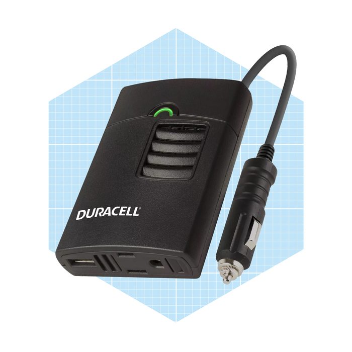 A black power adapter with a green light connects to a vehicle's power outlet, designed for charging devices in a vehicle.