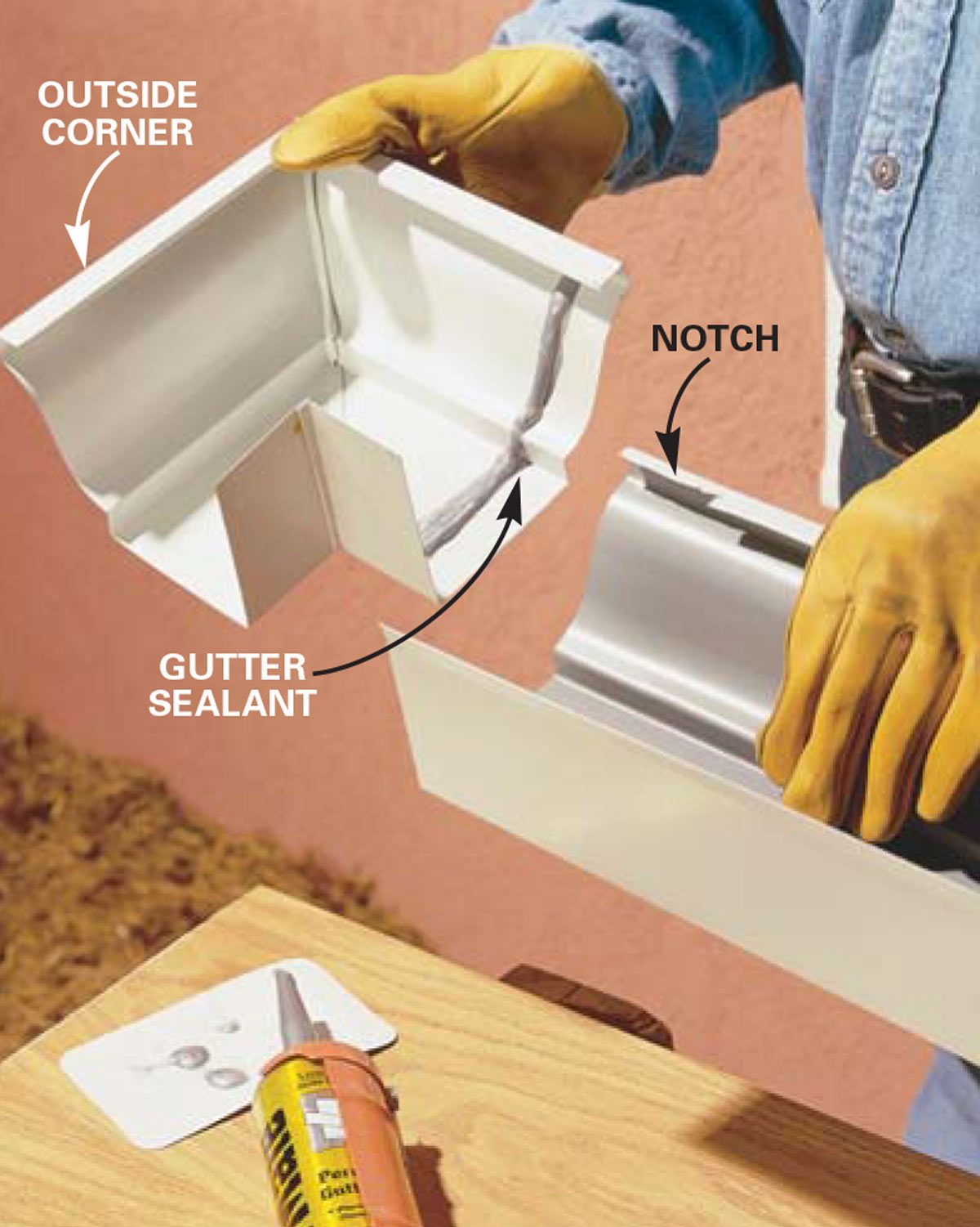 A person wearing gloves holds gutter pieces, aligning them for installation, with a backdrop of a peach-colored wall and a tube of sealant on a table.
