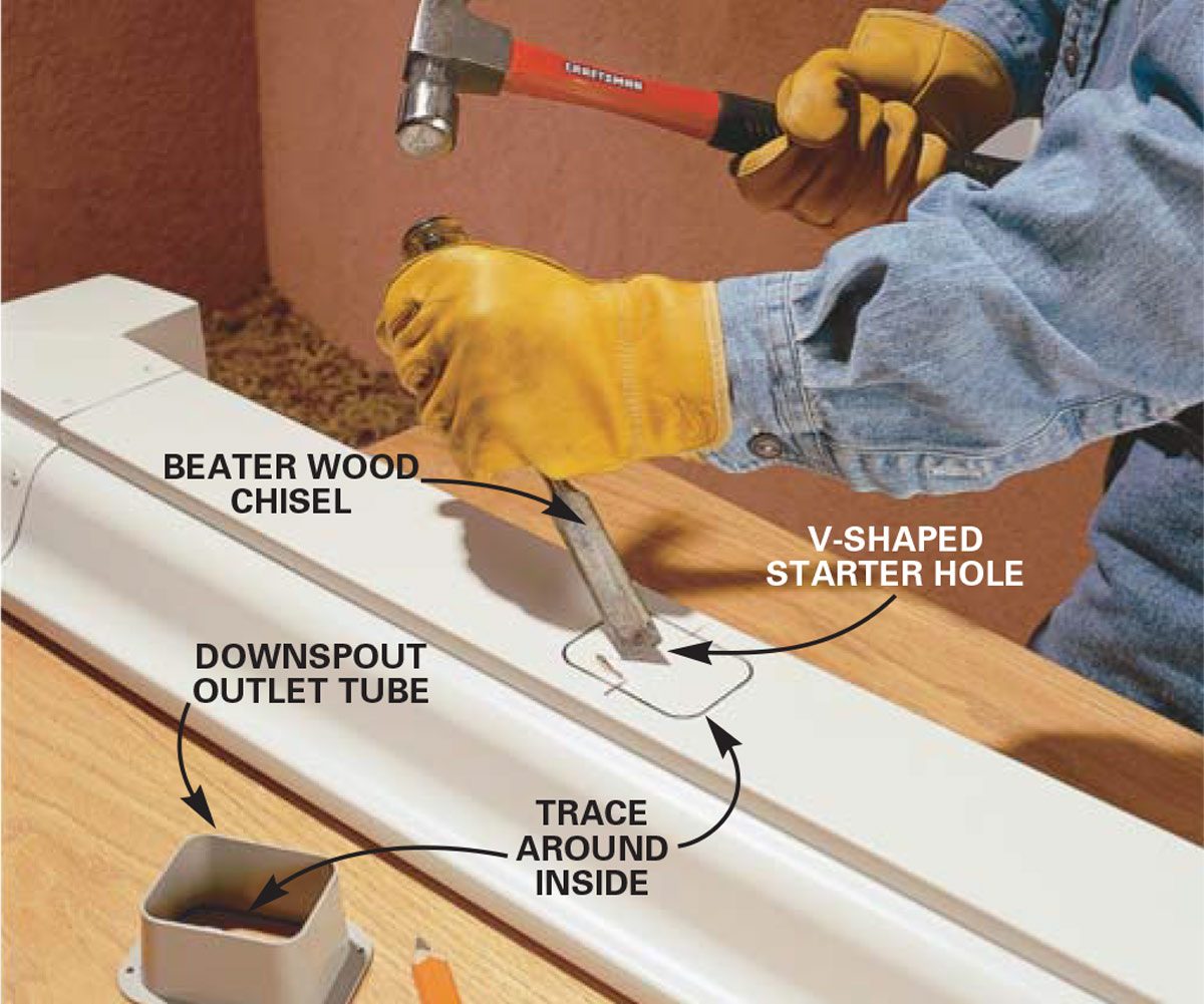 A gloved hand uses a chisel and hammer to create a V-shaped starter hole in a white piece of material, positioned on a wooden surface.