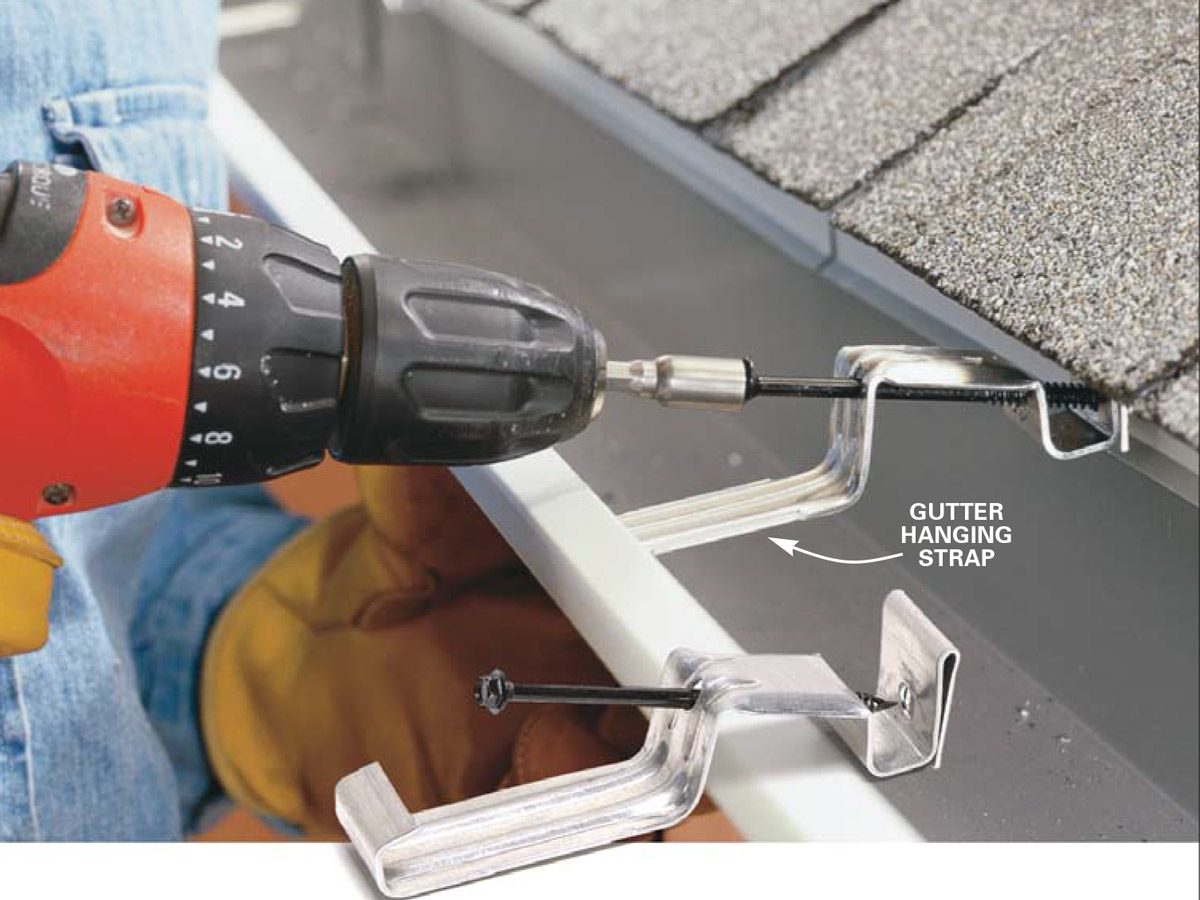 A drill attaches a gutter hanging strap to a roof, demonstrating a home improvement task with shingles and a gutter in the background.