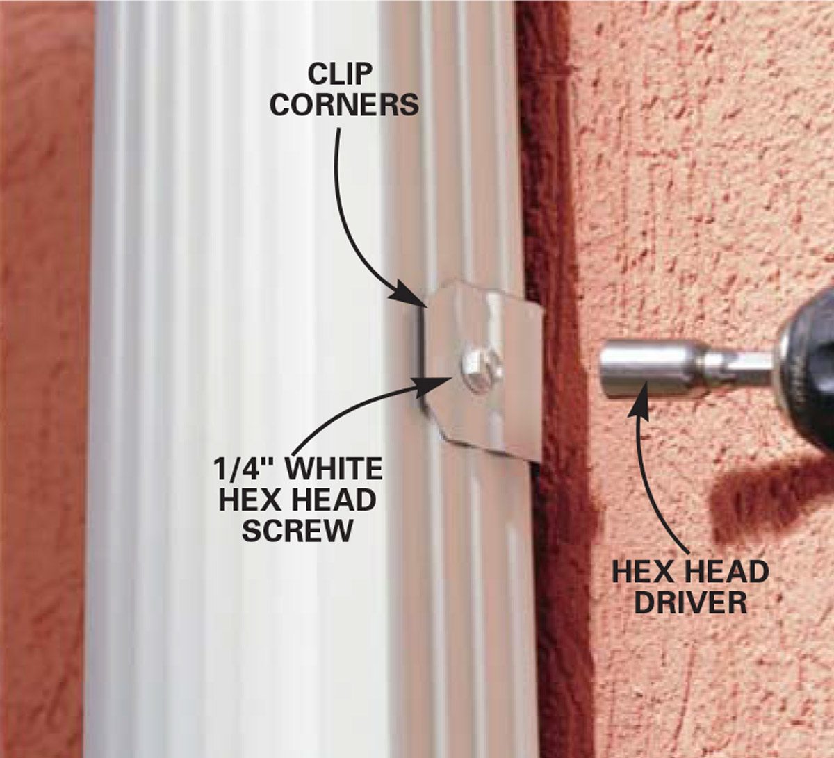 A metal clip secures corners of a white vertical object, with a hex head screw visible nearby and a hex head driver in action against a textured wall.