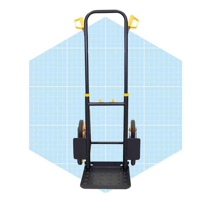 A hand truck stands upright with two wheels and a flat base, designed for transporting items, set against a light blue geometric background.