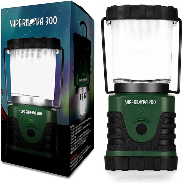 A green lantern emits light, poised next to its colorful packaging, showcasing features and branding, suggesting utility for outdoor or emergency situations.