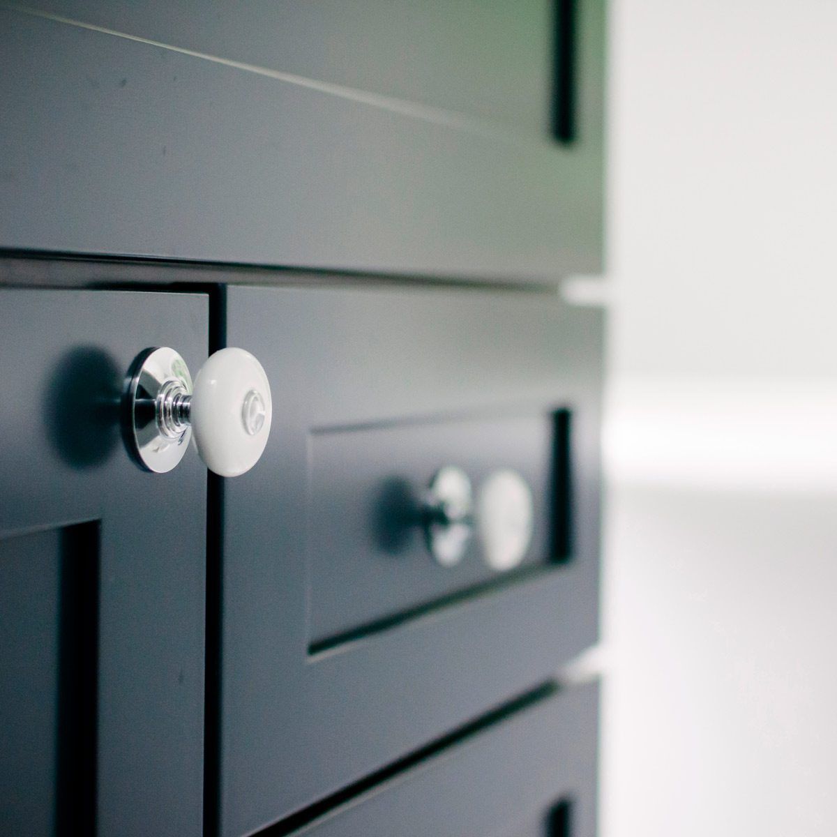 A black cabinet features shiny, round knobs; one is white while others are silver. The setting is minimalistic with a light, neutral background.