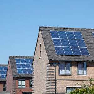 Houses feature solar panels on sloped roofs under a clear blue sky, with street lamps and windows visible, indicating a residential neighborhood.