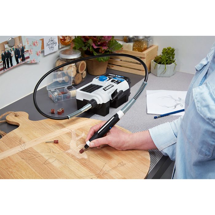 A person uses a wood-burning tool to create designs on a wooden board in a crafting area surrounded by tools and decor.