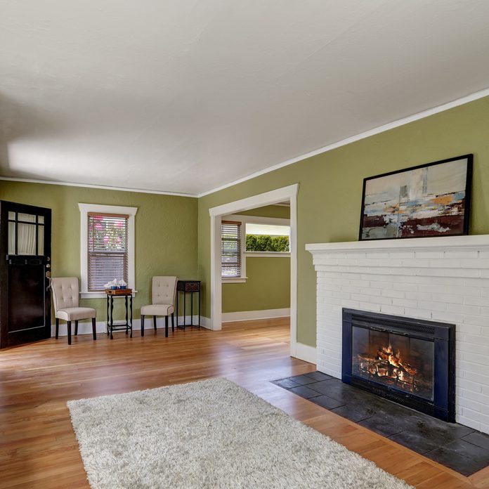 Living-room-interior-design-of-craftsman-home-with-white-brick-fireplace-built-in-shelves-window-seat-with-pillows-pale-green-walls-and-hardwood-floor